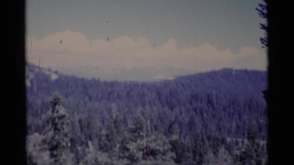 Final 8mm frame of the California wilderness panorama, with layered forest ridges, pale clouds, and dark scan borders.
