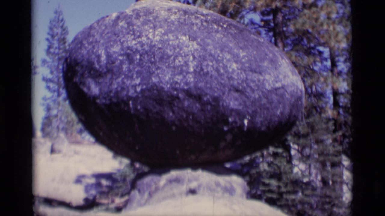 Balanced boulder in a forest clearing with dark film borders visible.
