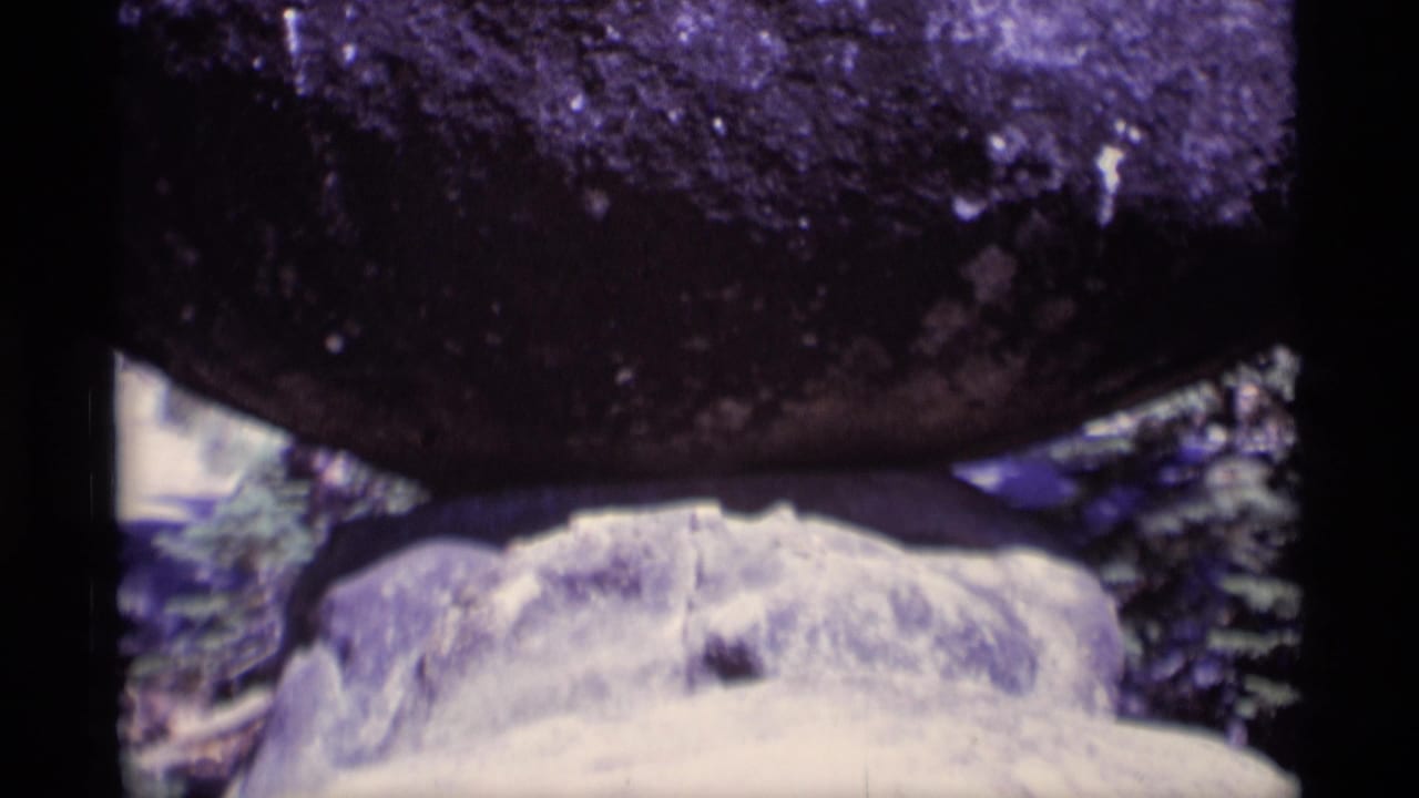 1975 8mm frame from Minaret Wilderness showing a close, soft-focused view of dark rock over pale stone and surrounding trees.