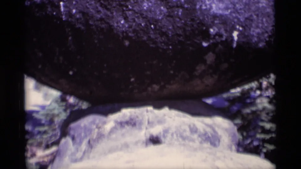 1975 8mm frame from Minaret Wilderness showing a close, soft-focused view of dark rock over pale stone and surrounding trees.