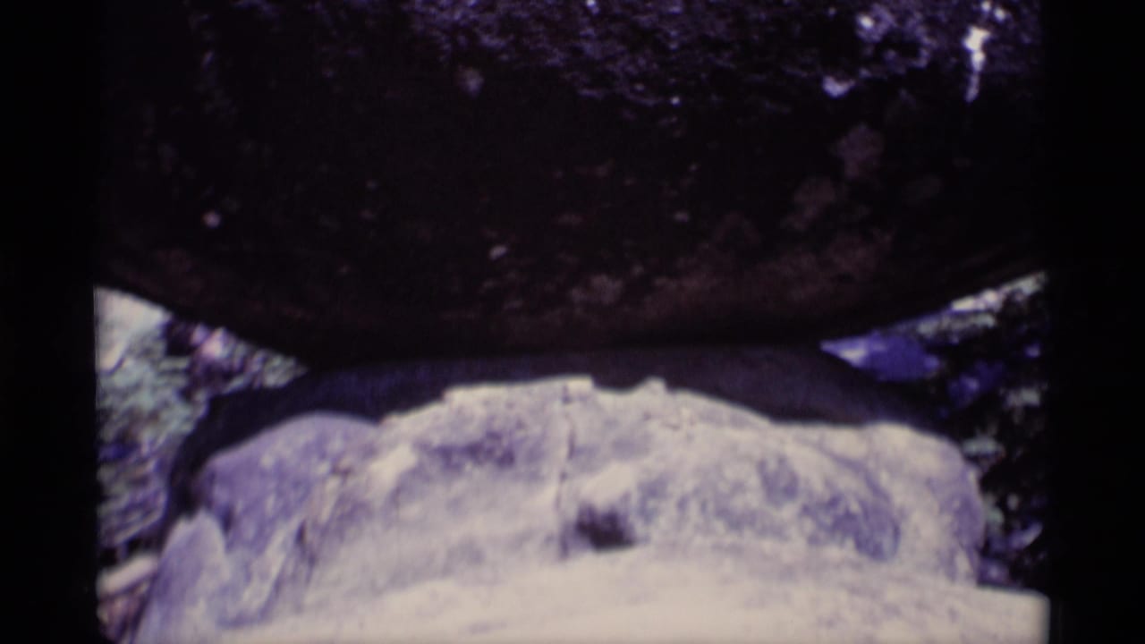 Close 1975 8mm view of a dark rock mass above pale stone, framed by trees in the Minaret Wilderness clip.