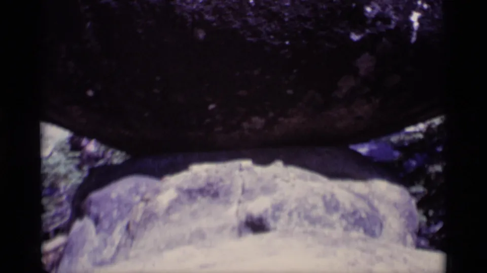 Close 1975 8mm view of a dark rock mass above pale stone, framed by trees in the Minaret Wilderness clip.
