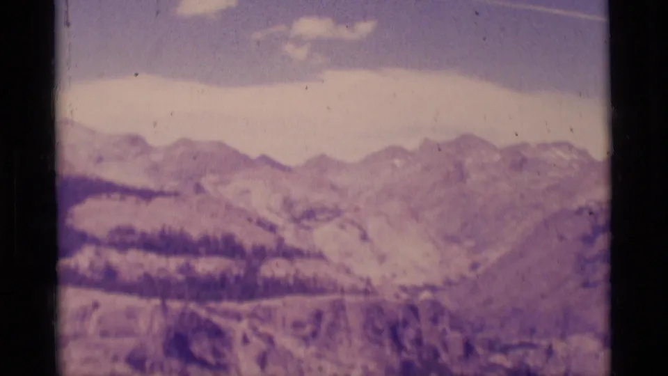 1975 8mm panorama of Minaret Wilderness ridgelines with snow patches, pale sky, and soft archival color.