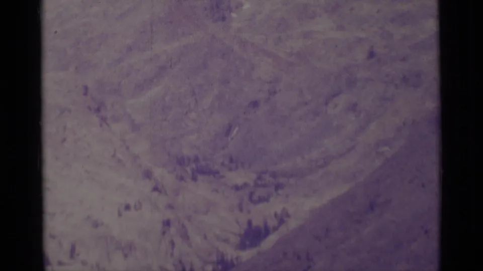 1975 Minaret Wilderness frame with rocky basin-like slopes, faint snow, dark trees, and visible 8mm film texture.