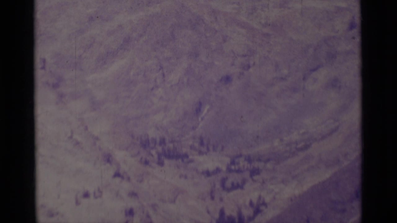 1975 Minaret Wilderness home-movie frame showing a hazy mountain slope, scattered forest, and aged 8mm color shift.