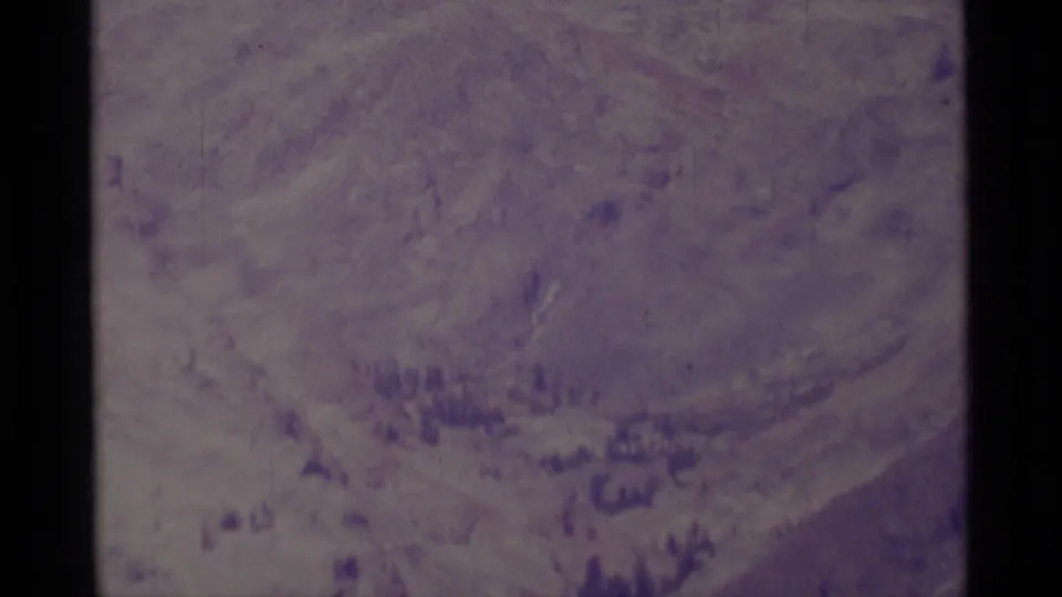 1975 Minaret Wilderness home-movie frame showing a hazy mountain slope, scattered forest, and aged 8mm color shift.