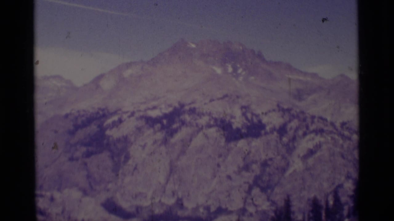1975 Minaret Wilderness frame with a snow-patched peak, rugged ridges, forest bands, and soft 8mm texture.