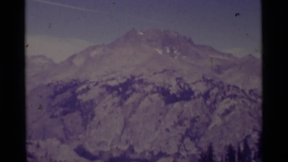 1975 Minaret Wilderness frame with a snow-patched peak, rugged ridges, forest bands, and soft 8mm texture.