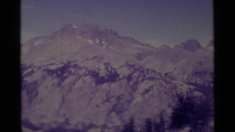 1975 8mm view of Minaret Wilderness ridges, snow patches, and forested slopes in muted purple color.