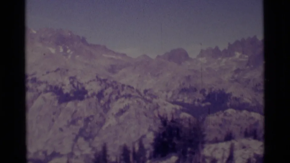 1975 Minaret Wilderness frame showing distant ridgelines, evergreen forest, snow patches, and aged 8mm borders.