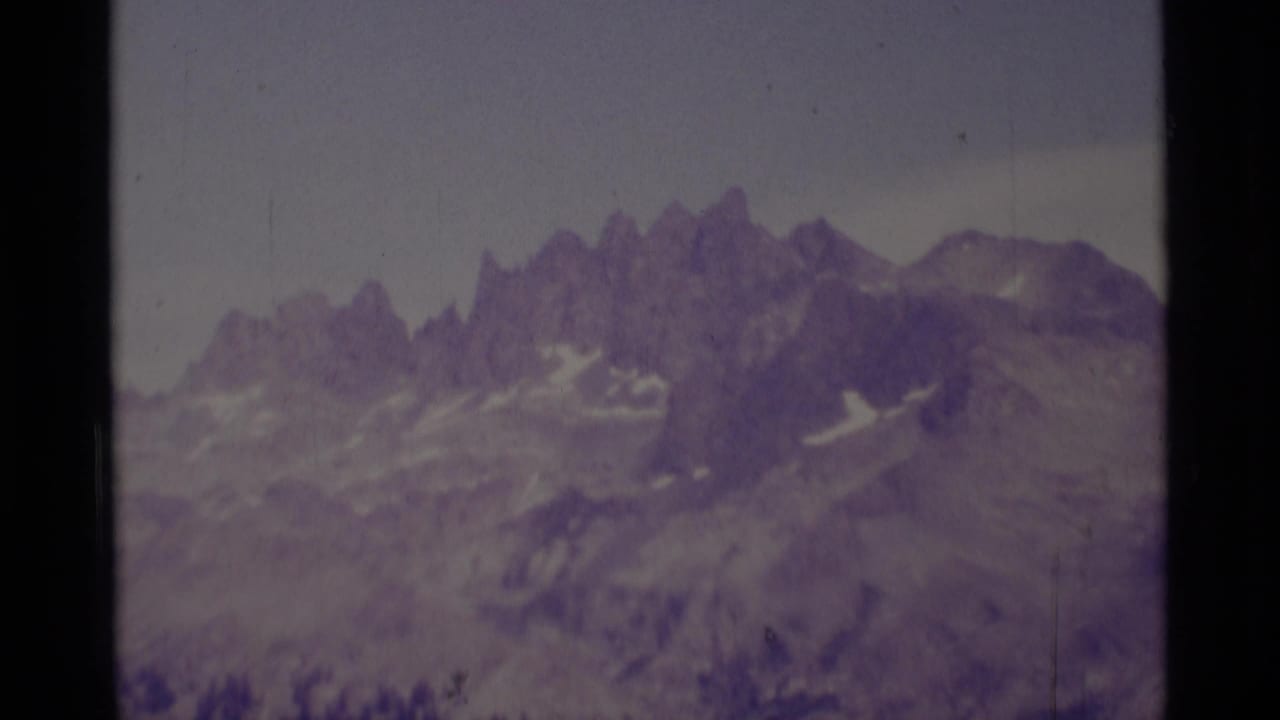1975 8mm view of rugged Sierra Nevada peaks in the Minaret Wilderness, with snow patches and a soft purple film cast.