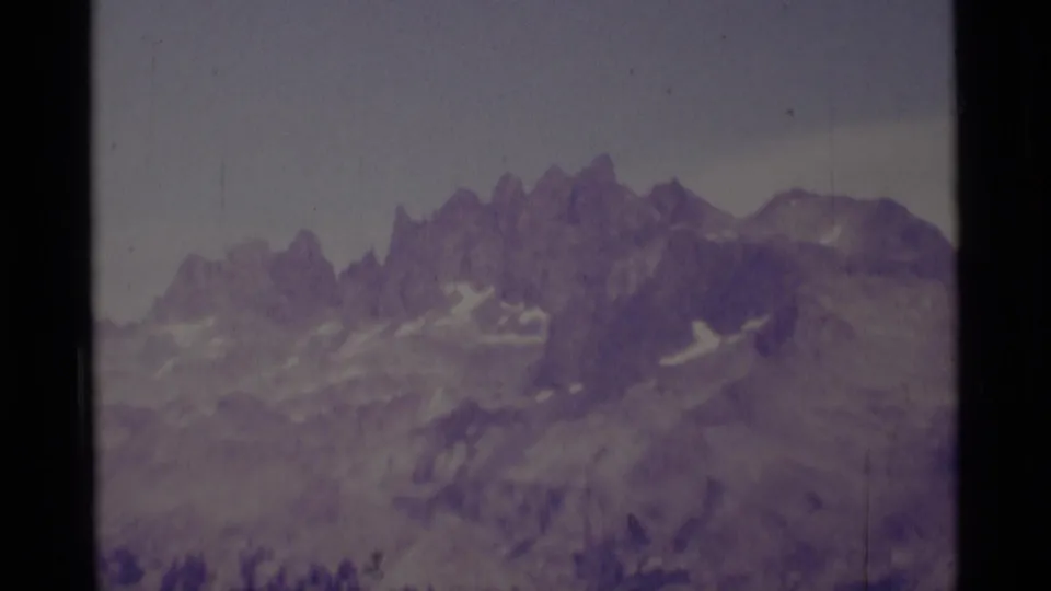 1975 8mm view of rugged Sierra Nevada peaks in the Minaret Wilderness, with snow patches and a soft purple film cast.