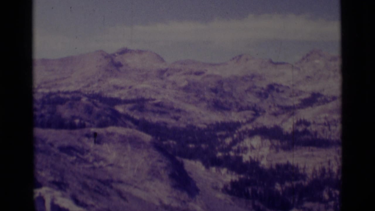 Snowy mountain ridges and forested slopes beneath thin clouds.