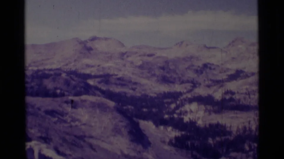 Distant snow-covered ridges and forested high country in the Minaret Wilderness, captured on purple-shifted 8mm film.