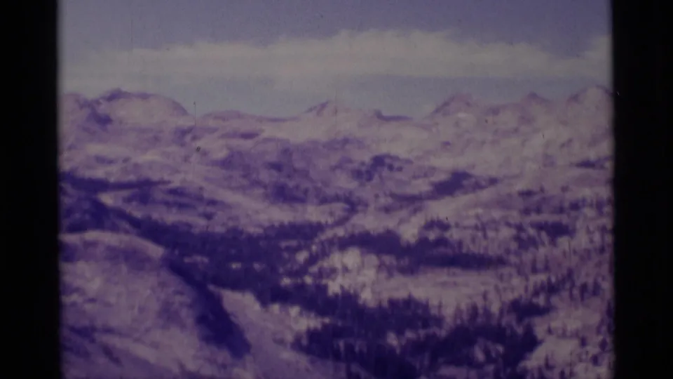 Wide 1975 home-movie panorama of Sierra Nevada ridges, snowfields, and dark forested slopes in the Minaret Wilderness area.