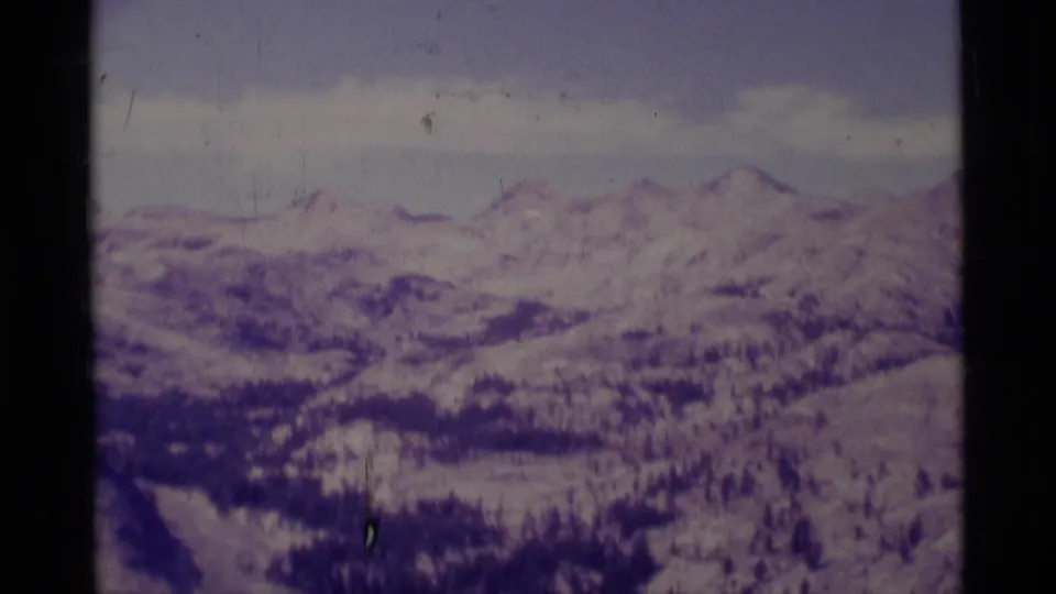 Soft 8mm frame of distant Minaret Wilderness peaks, snow-streaked terrain, forest bands, and a pale clouded sky.