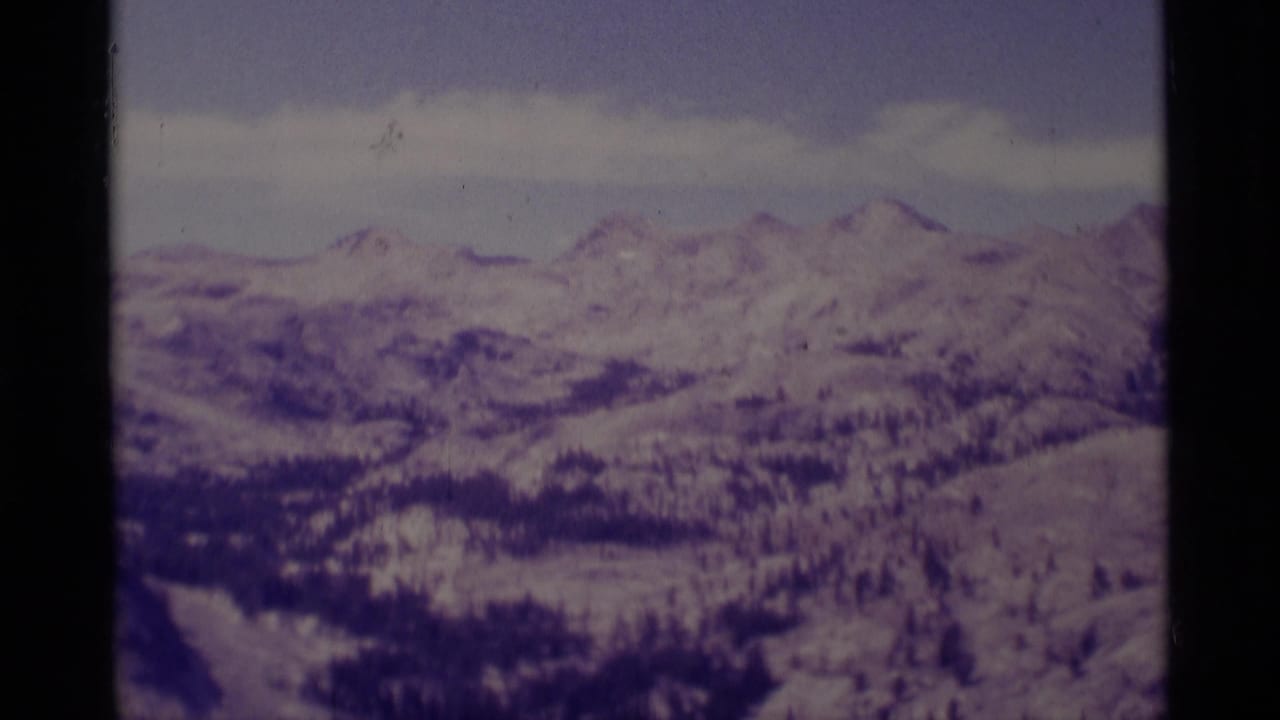1975 8mm view of the Minaret Wilderness area, showing distant snowy ridges and dark evergreen bands with a purple film cast.