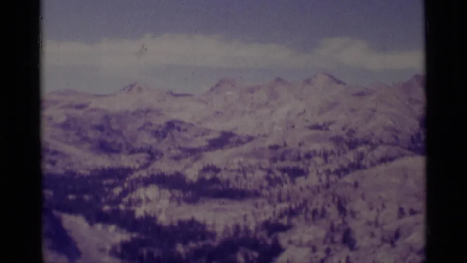 1975 8mm view of the Minaret Wilderness area, showing distant snowy ridges and dark evergreen bands with a purple film cast.