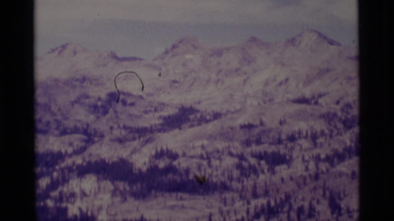 1975 8mm frame of Minaret Wilderness mountain terrain, with snowy peaks, evergreen patches, and visible scan scratches.