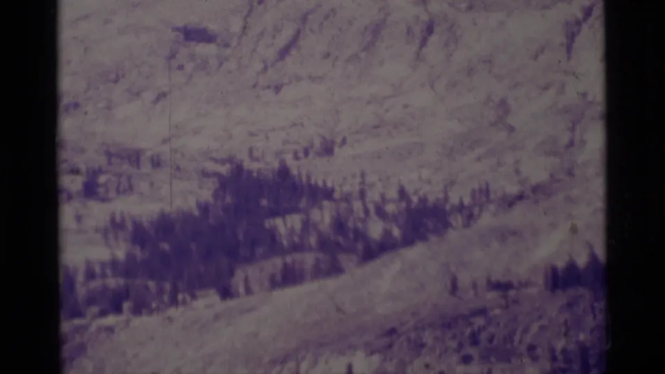 Late-frame 1975 8mm view of Minaret Wilderness terrain, showing a zoomed valley, snowy slopes, and dark forest patches.