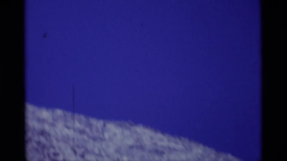 A rugged Minaret Wilderness slope sits low in frame beneath a saturated blue sky in 1975 8mm footage.
