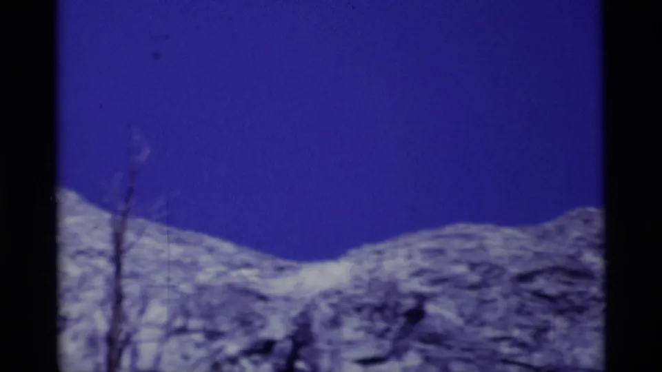 Rocky California wilderness terrain and a bare tree appear below a deep blue sky in this 1975 8mm frame.