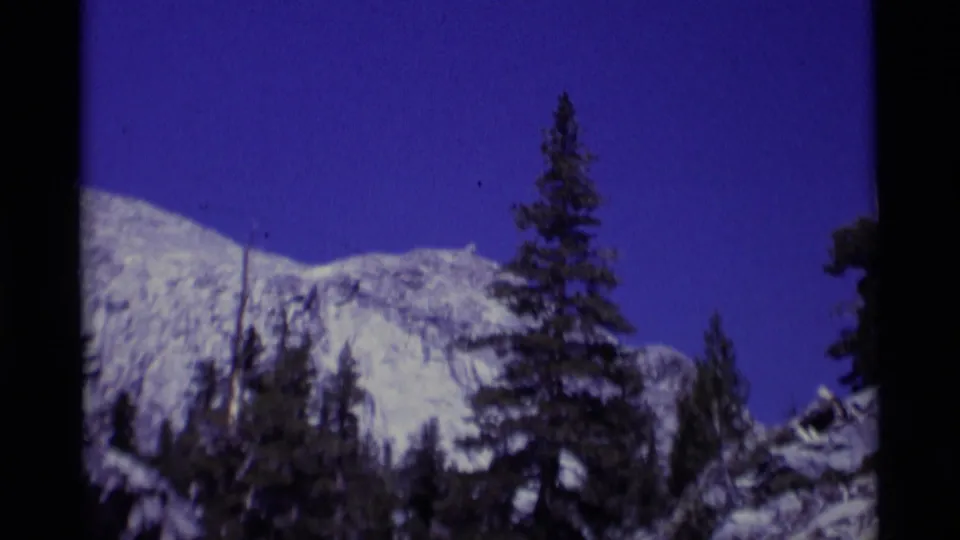 1975 8mm California wilderness view of distant rock slopes and pine trees, with visible grain and dark scan edges.
