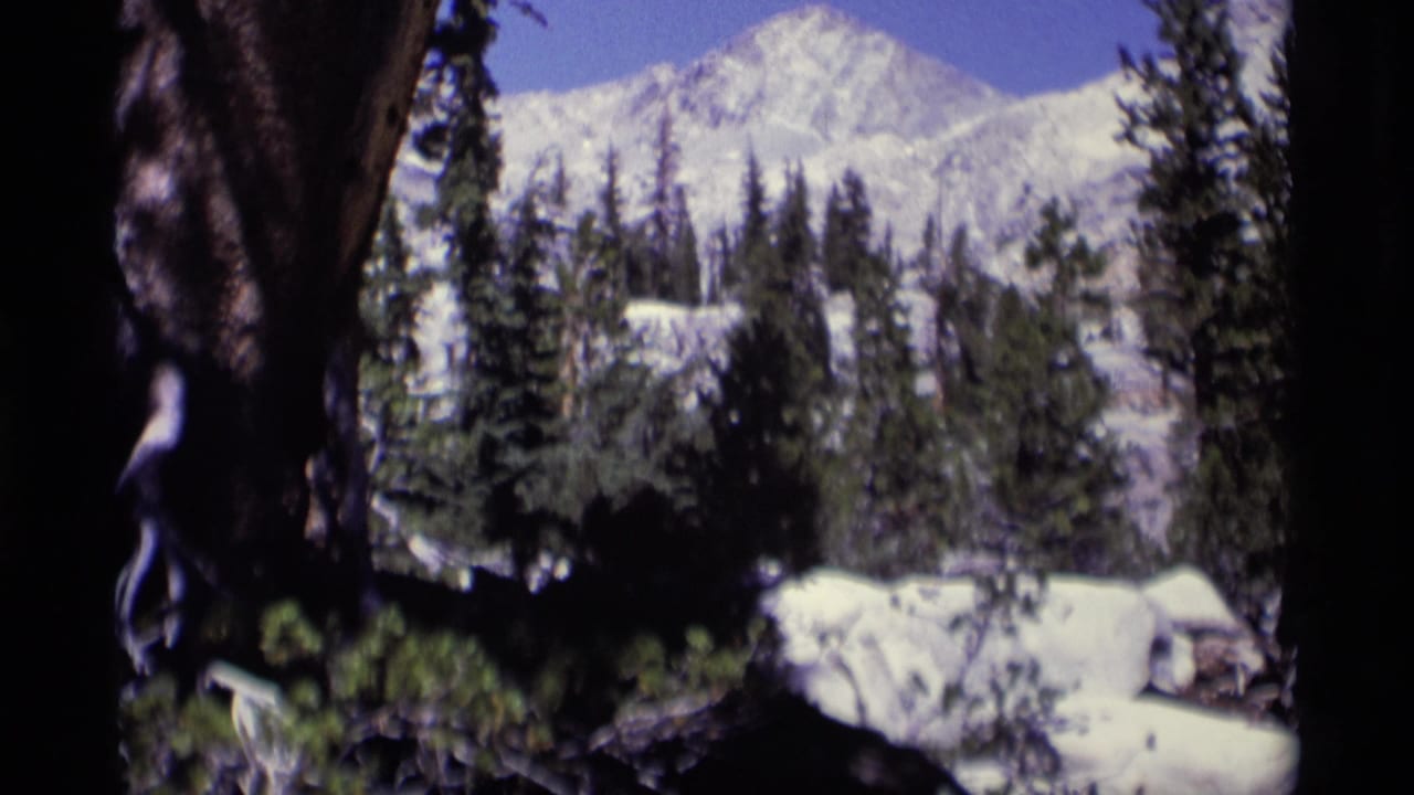 Handheld 8mm frame of the Minaret Wilderness landscape with snow, conifers, rocks, and strong shaded foreground shapes.