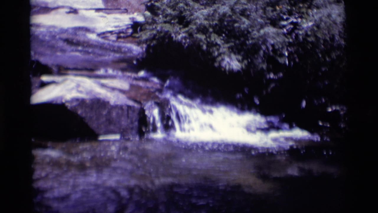 Small waterfall spilling over rock ledges beneath dark trees.