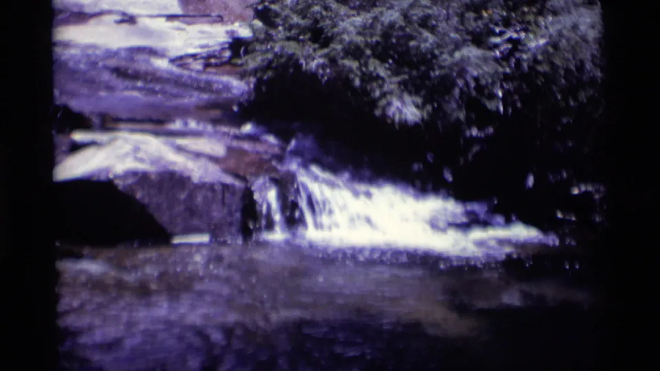 1975 8mm Minaret Wilderness frame showing water cascading over layered rocks under shaded tree cover.