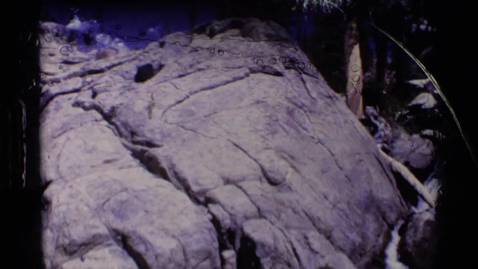 1975 Minaret Wilderness 8mm frame showing a dry cracked rock surface near shaded branches and streamside growth.