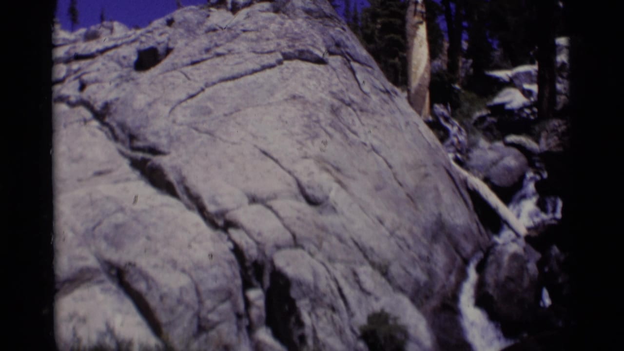 1975 8mm frame from Minaret Wilderness showing whitewater moving through granite rocks with forest shadows behind it.