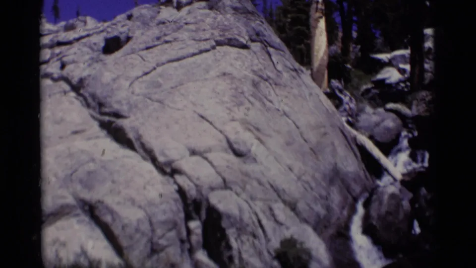 1975 8mm frame from Minaret Wilderness showing whitewater moving through granite rocks with forest shadows behind it.