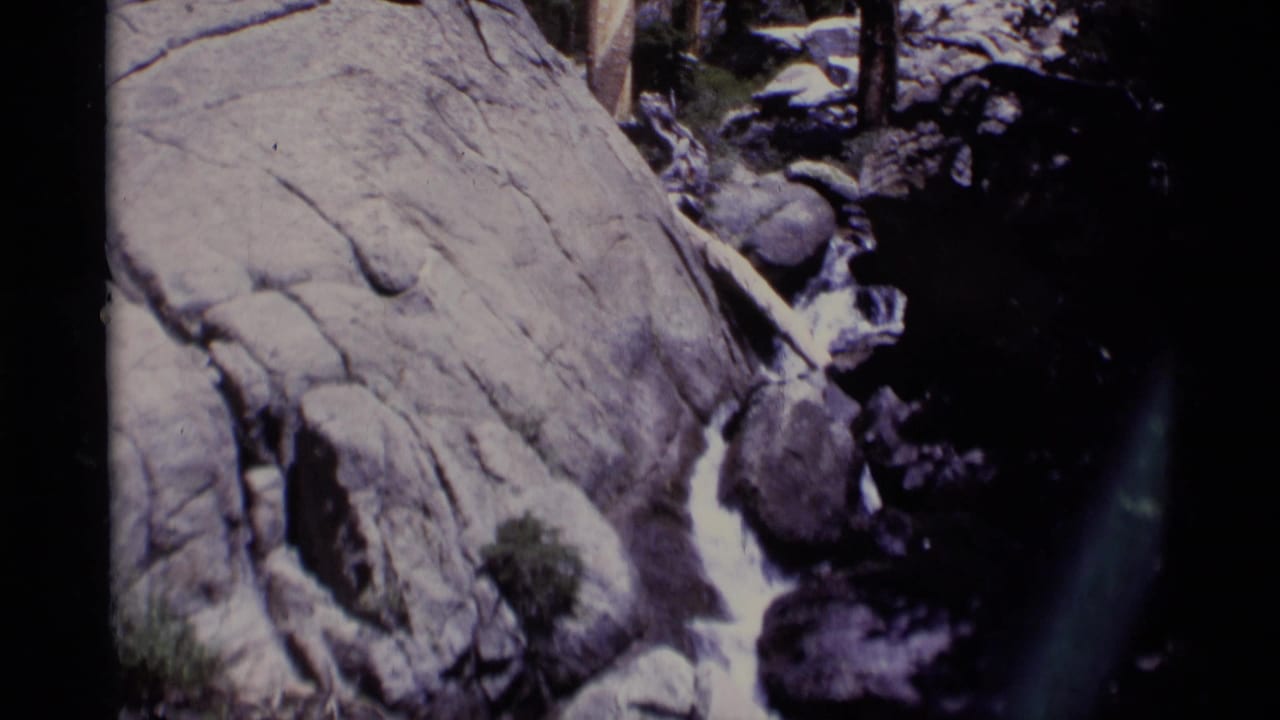 Minaret Wilderness stream frame with rushing water pressed between pale granite and darker boulders in a handheld 8mm view.