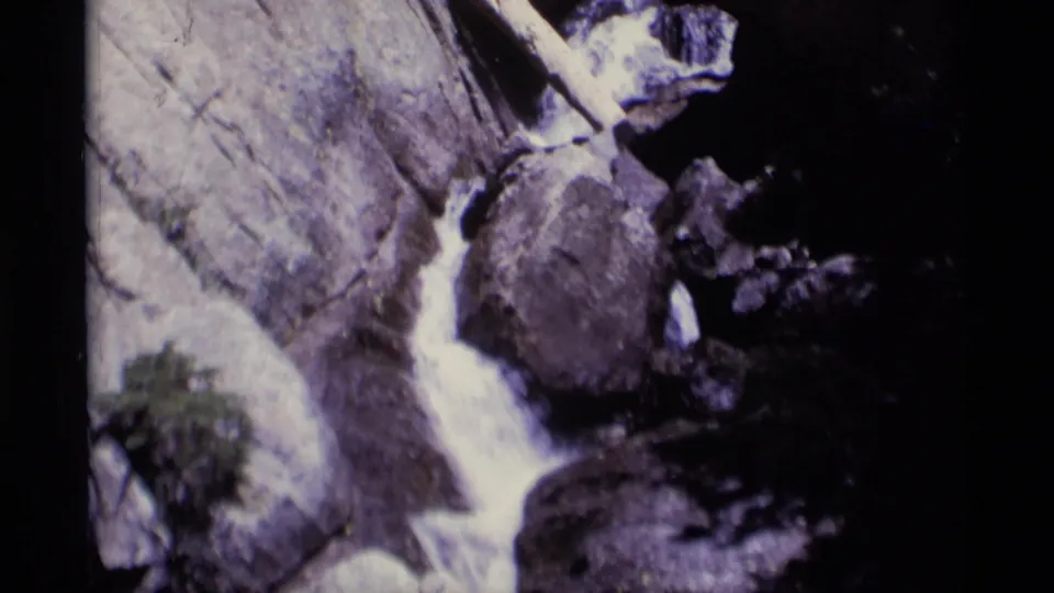 Final 8mm frame of the Minaret Wilderness stream with bright water crossing between boulders and dark terrain at the right edge.
