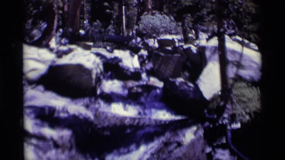 1975 8mm view of a rocky stream in the Minaret Wilderness, with white water crossing dark boulders under forest shade.