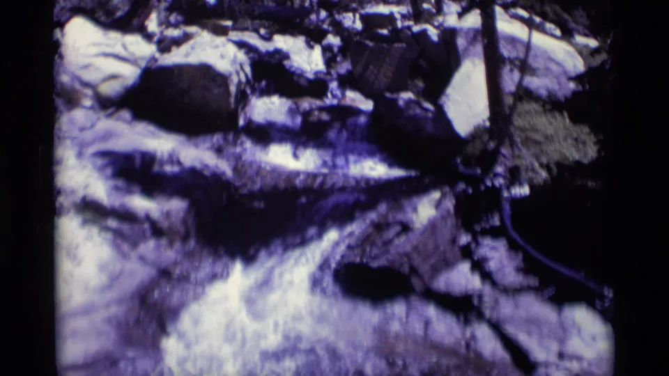 Rocky Minaret Wilderness stream on 8mm film, with pale froth, dark stones, and shaded trees around the channel.