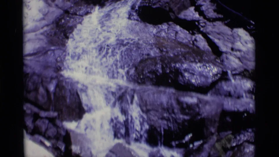 1975 home-movie frame of white water churning around rocks in the Minaret Wilderness, with strong blue-purple film aging.