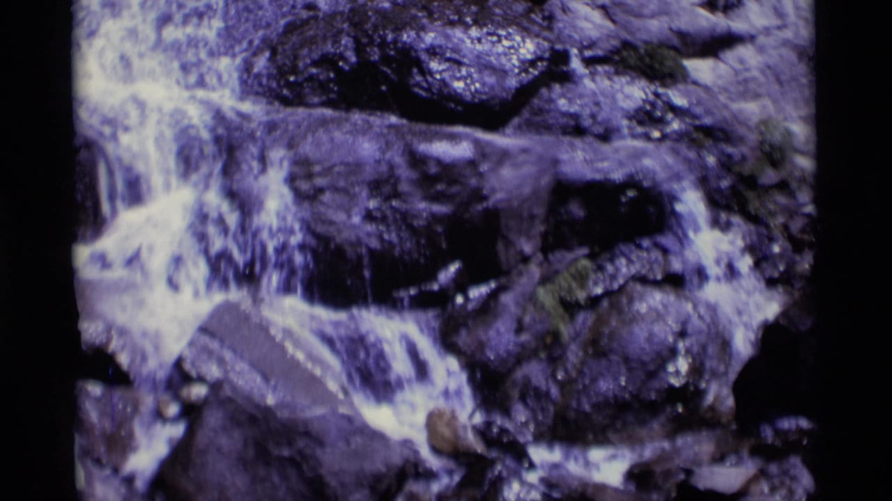 Vintage 8mm frame showing a small waterfall or stream drop over dark rocks in the California wilderness location identified by metadata.