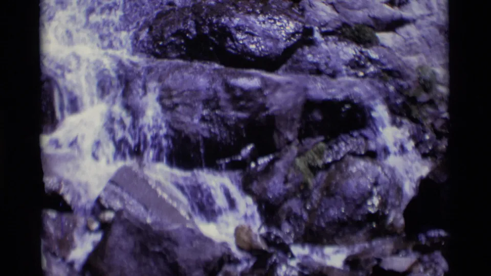 Vintage 8mm frame showing a small waterfall or stream drop over dark rocks in the California wilderness location identified by metadata.