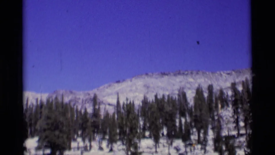 1975 8mm view of a snow-dusted mountain slope and evergreen forest in the Minaret Wilderness area.