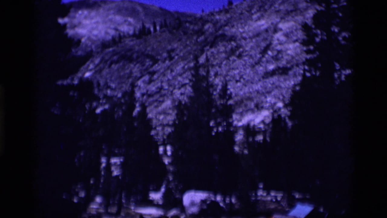 Minaret Wilderness mountain forest with snow patches, pines, and strong blue-purple 8mm color shift in a 1975 home-movie frame.