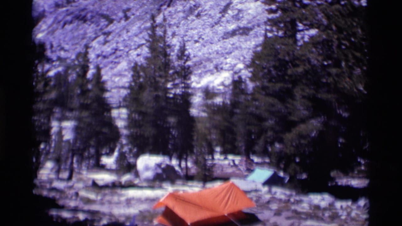 1975 Minaret Wilderness camping scene with an orange tent, green tarp, snow patches, rocks, and pine trees.