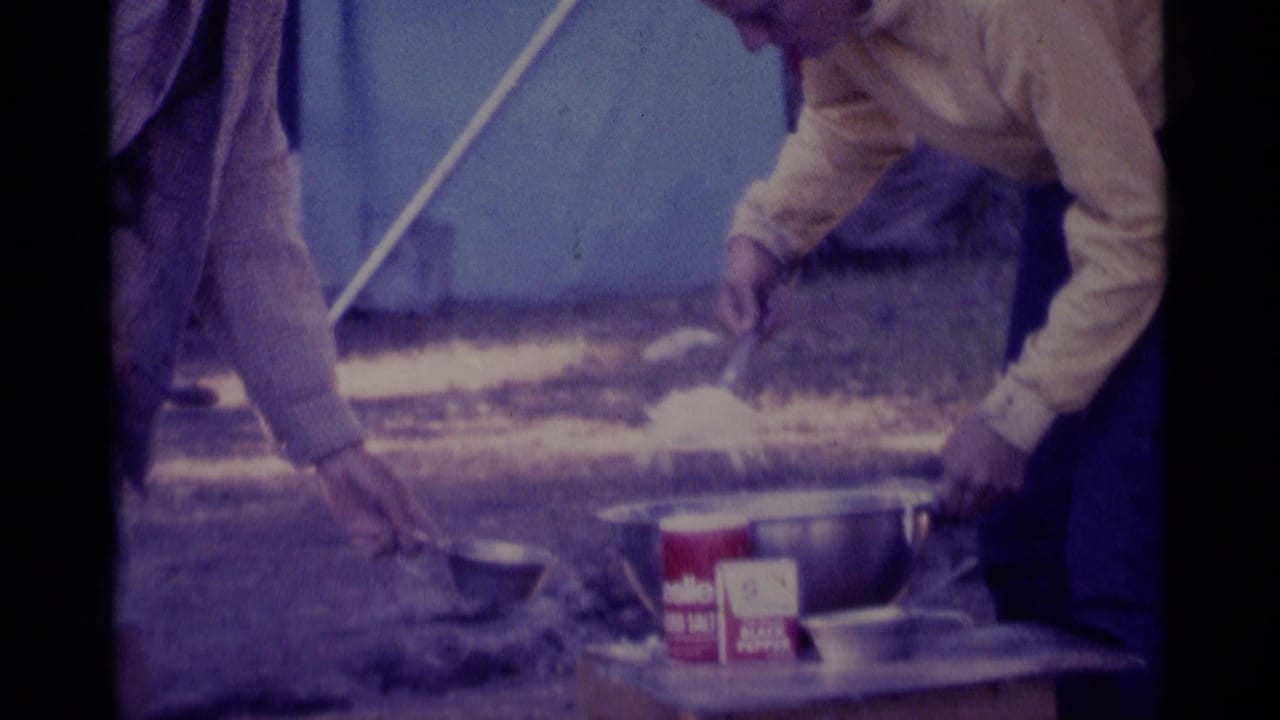 Close view of hands, a metal bowl, spoon, and seasoning container on a camp table.