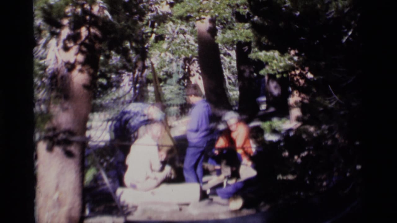 1975 8mm home-movie frame from Minaret Wilderness showing adults gathered casually in a shaded forest.