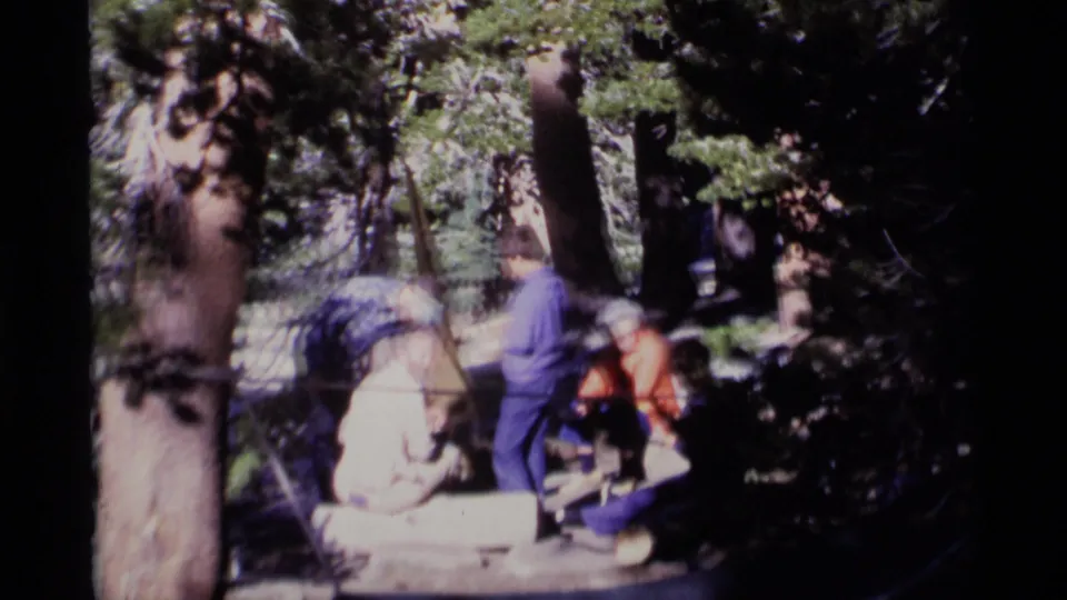 1975 8mm home-movie frame from Minaret Wilderness showing adults gathered casually in a shaded forest.