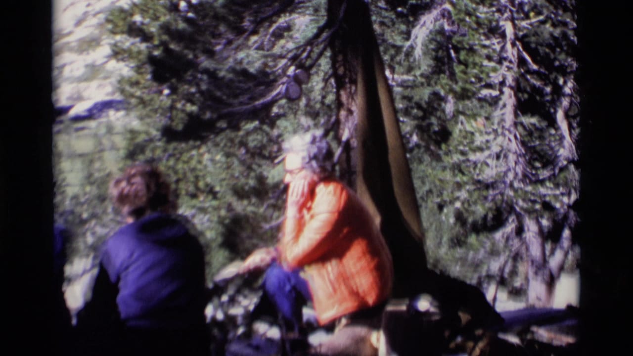 1975 8mm Minaret Wilderness frame showing campers seated by a tent among trees, with a woman in an orange jacket eating or resting.