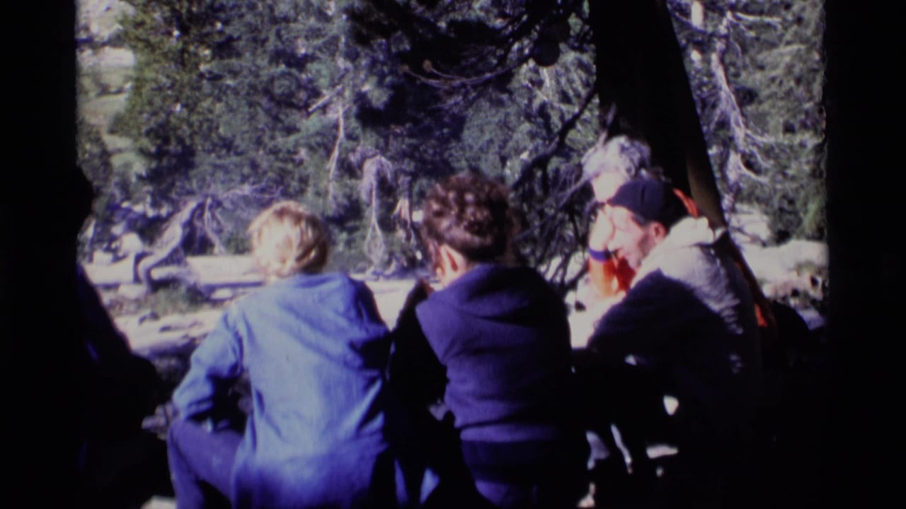1975 8mm home-movie frame of people sitting on a fallen log in Minaret Wilderness forest shade.
