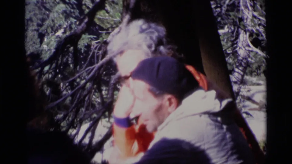Soft 8mm close view of an older man in a cap and light jacket sitting in a California forest setting.