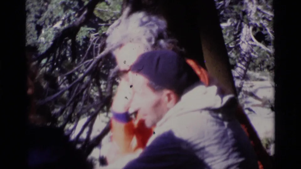 1975 8mm frame showing an older man in a cap seated with others under trees in Minaret Wilderness.